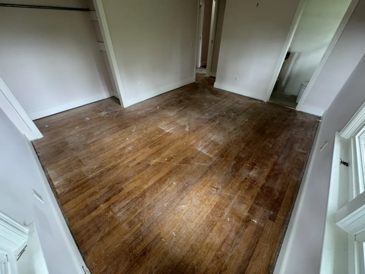 A bedroom hardwood floor worn and dull before refinishing